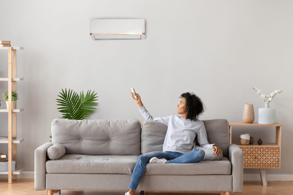 woman sat on the sofa pointing a remote at the air conditioning unit